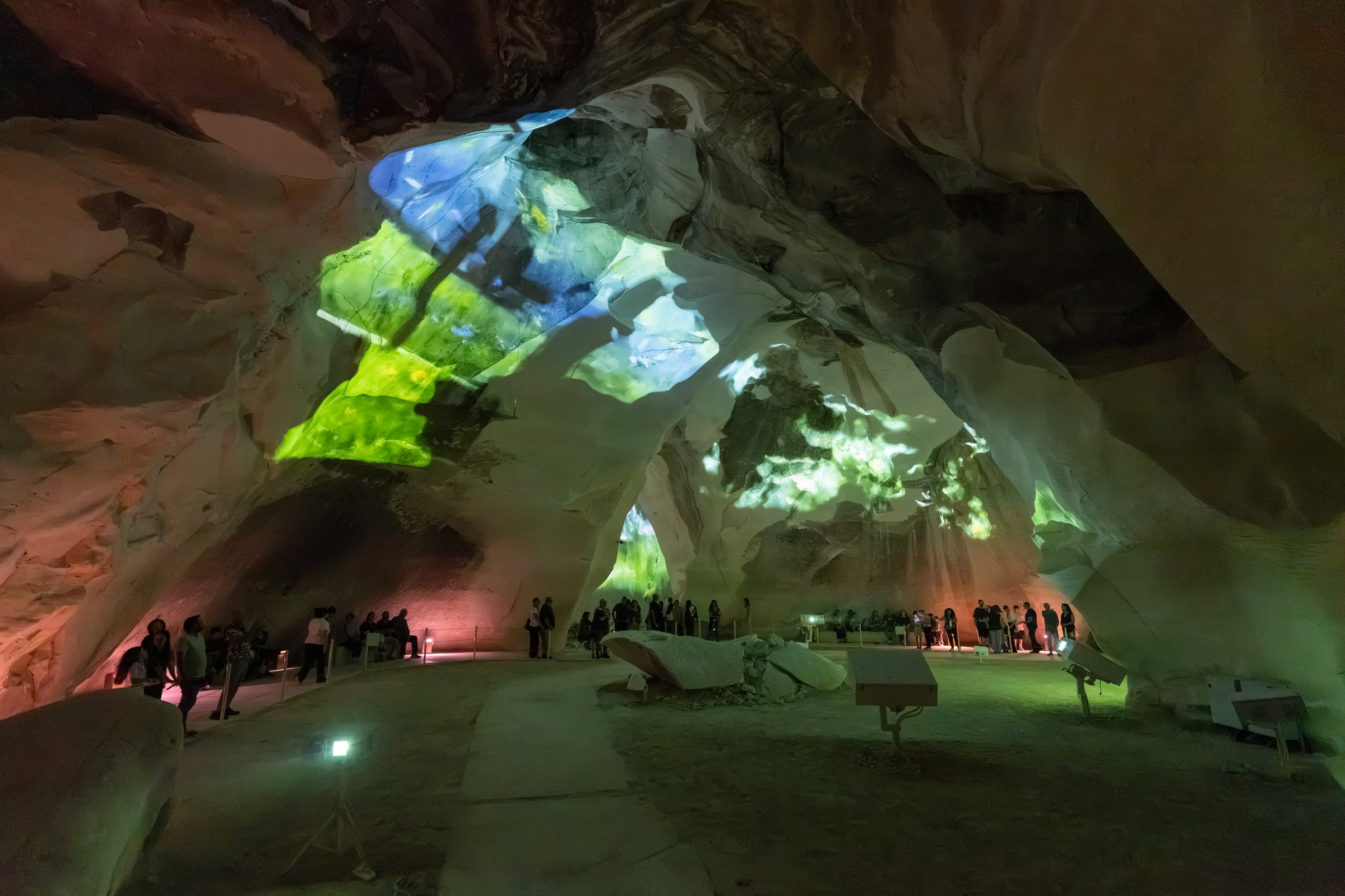 Green and pale blue projections fill the cavern above visitors watching from its perimeter.