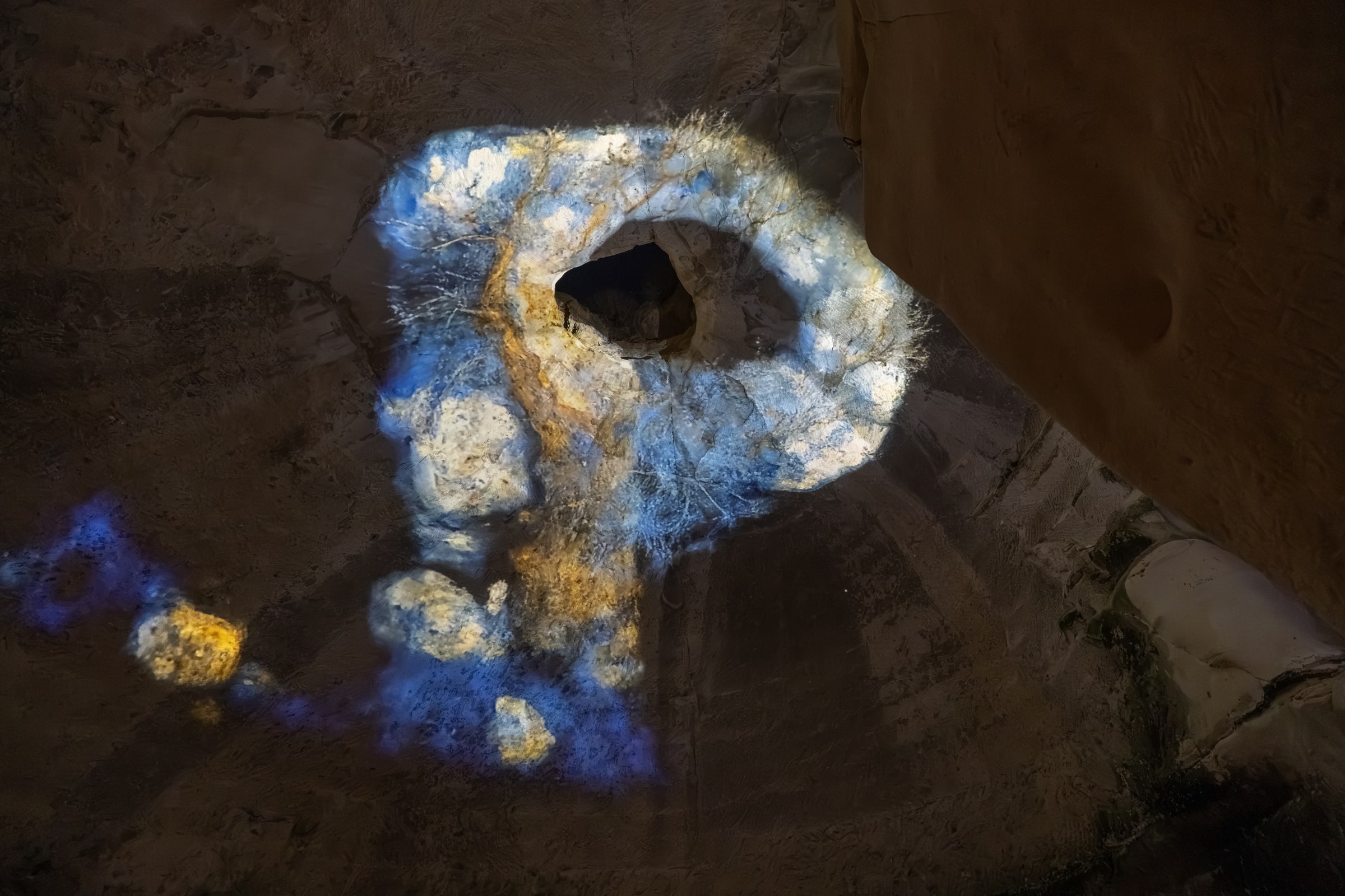 A blue, white and gold projected ring surrounds an opening in the stone ceiling.