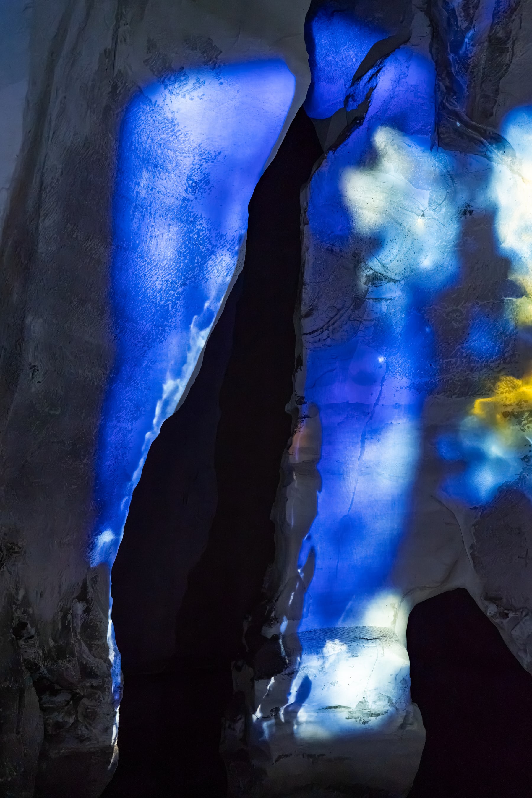 Electric-blue light traces a narrow fissure between rough stone surfaces.